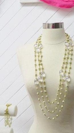 A mannequin displaying a multilayer pearl necklace and a matching bracelet with gold-plated wire on a white wooden background.