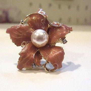A large brown flower-shaped ring with a floral design and a central pearl, surrounded by smaller clear stones set in gold-tone metal.