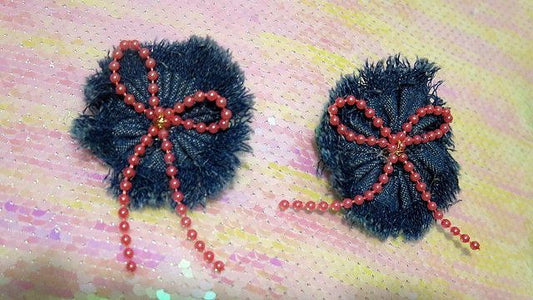 A pair of denim earrings with pink pearl bows and red embellishments.
