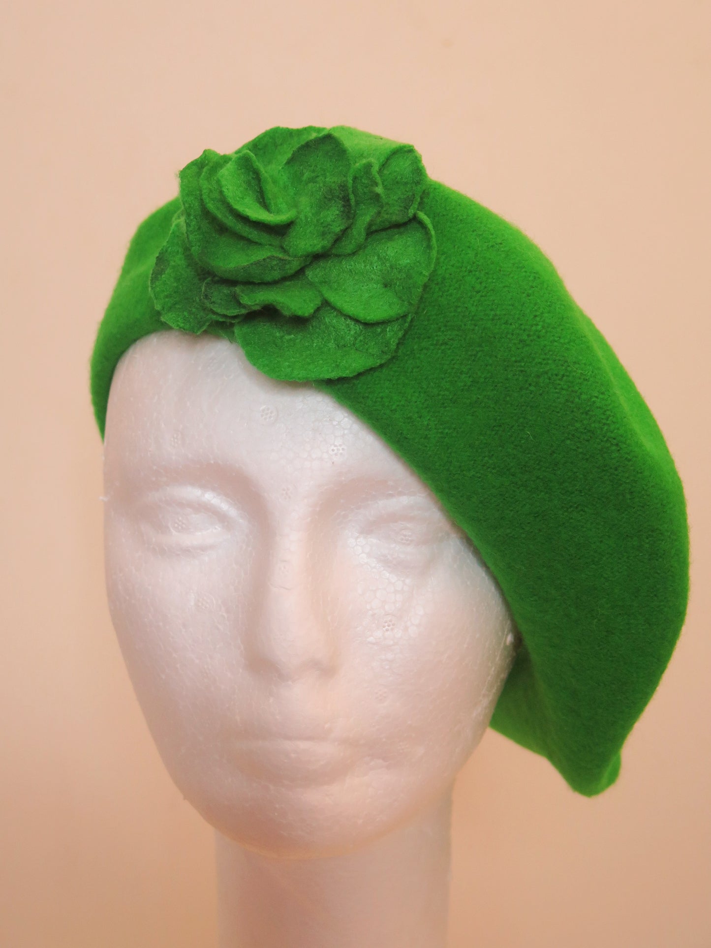 A green wool beret hat with a handcrafted felt flower on a mannequin head.