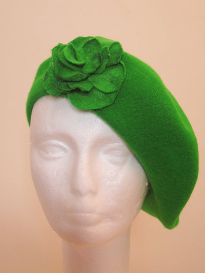 A green wool beret hat with a handcrafted felt flower on a mannequin head.