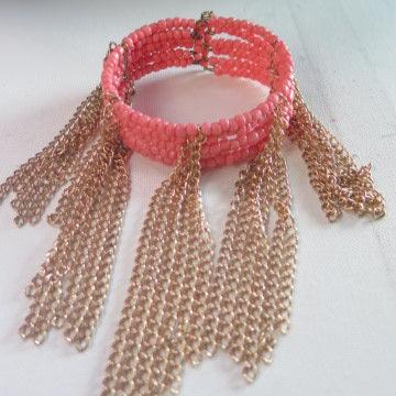A peach pink cuff bracelet with gold fringe accents, featuring intricate gold chain details and pink seed beads.