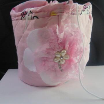 A pink fabric toiletry bag with a 3D flower detail and a pull-string closure.