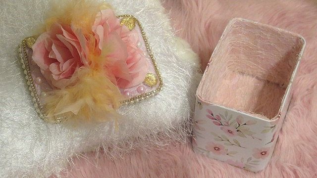 A pink Victorian-style jewelry box with floral patterns and a feathered embellishment on top.
