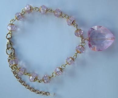 A pink heart-shaped bracelet with a gold chain and clear beads, featuring a polished finish and a lobster clasp.