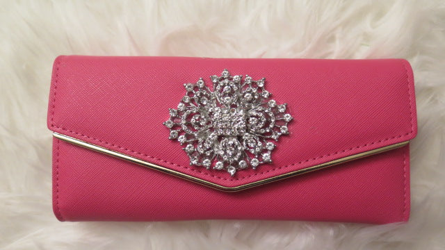A pink leather wallet with a decorative element featuring sparkling rhinestones on the flap.