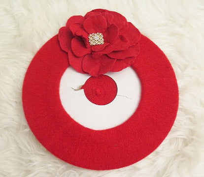 A red wool beret with a decorative felt flower on top.