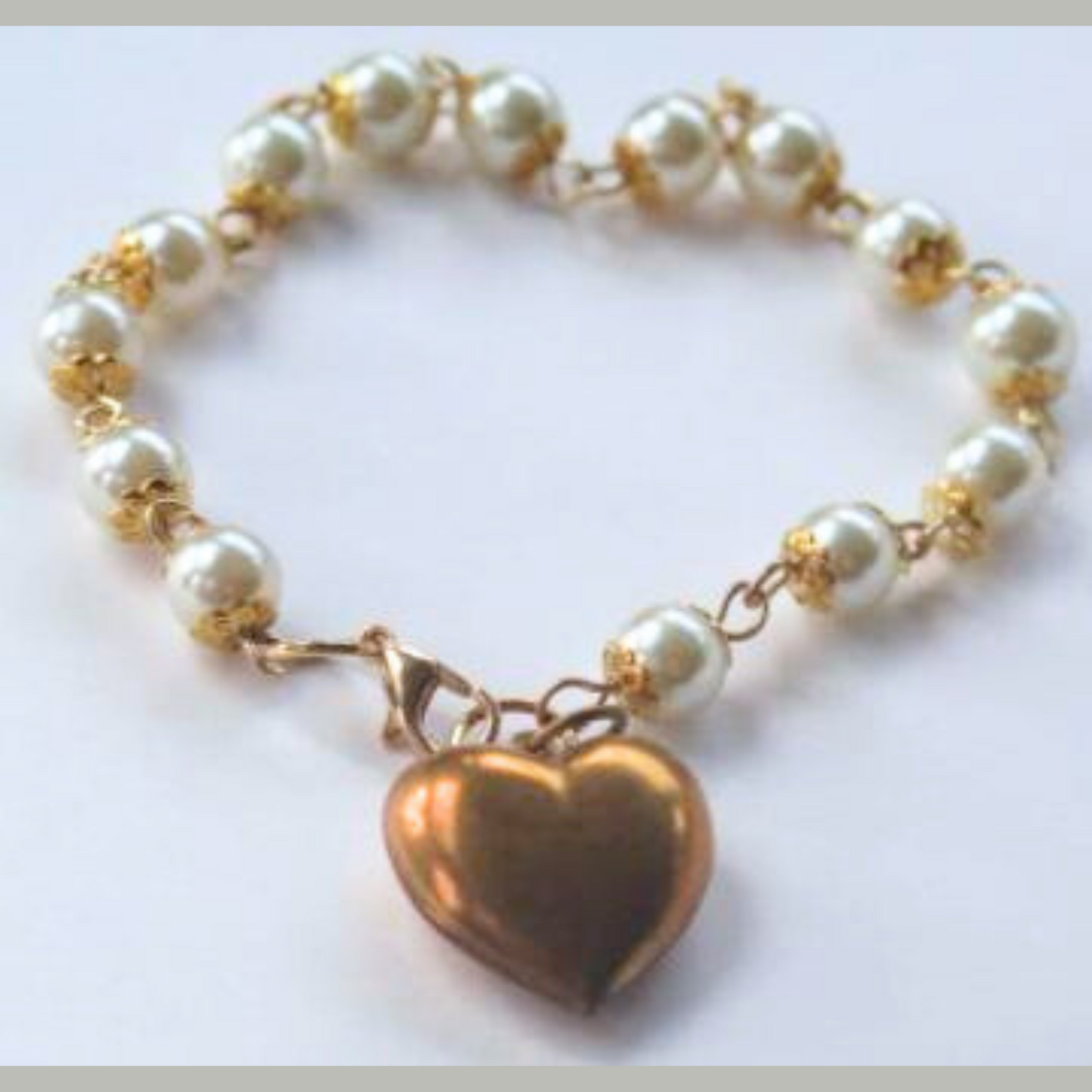 Bracelet with white pearls and gold wiring, featuring a gold heart-shaped charm.