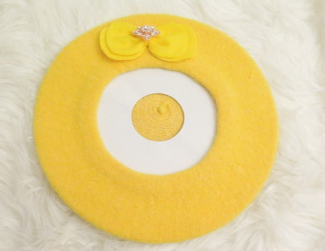 A yellow wool beret with a bow and a rhinestone on it.