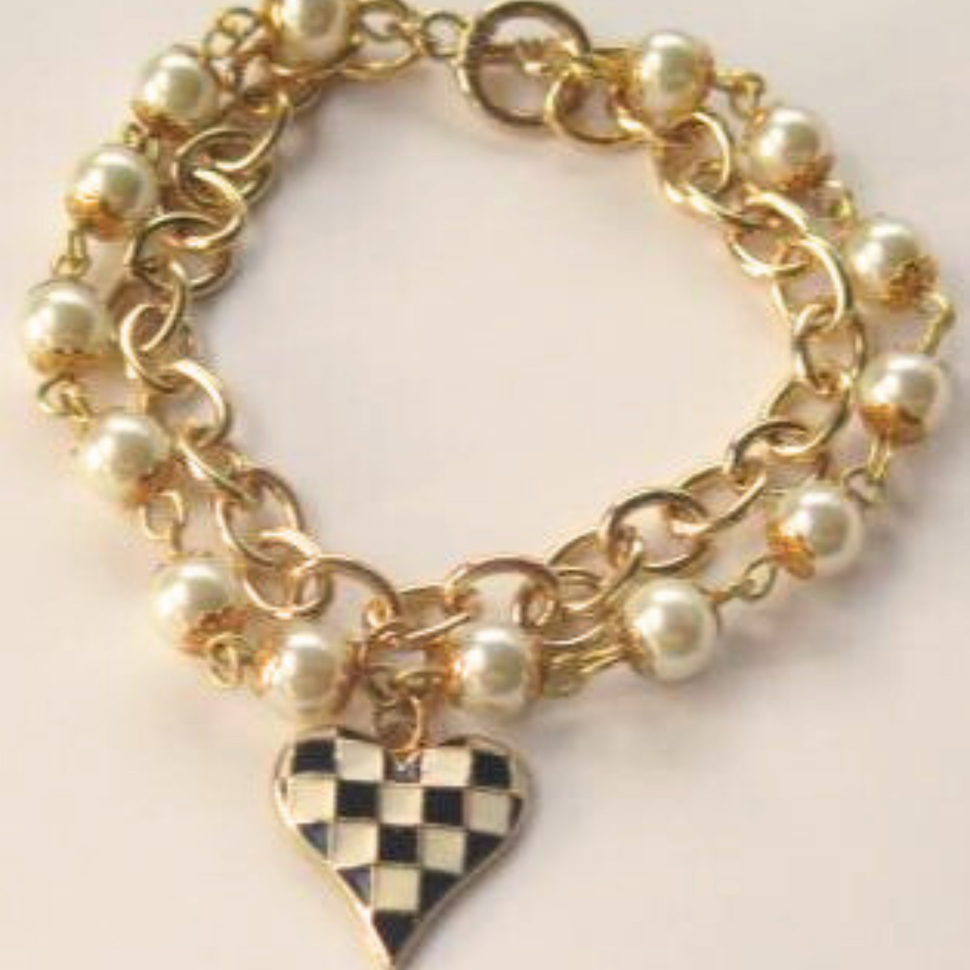 double strand pearl and gold chain bracelet with a black and white checkered heart charm attached to the center.